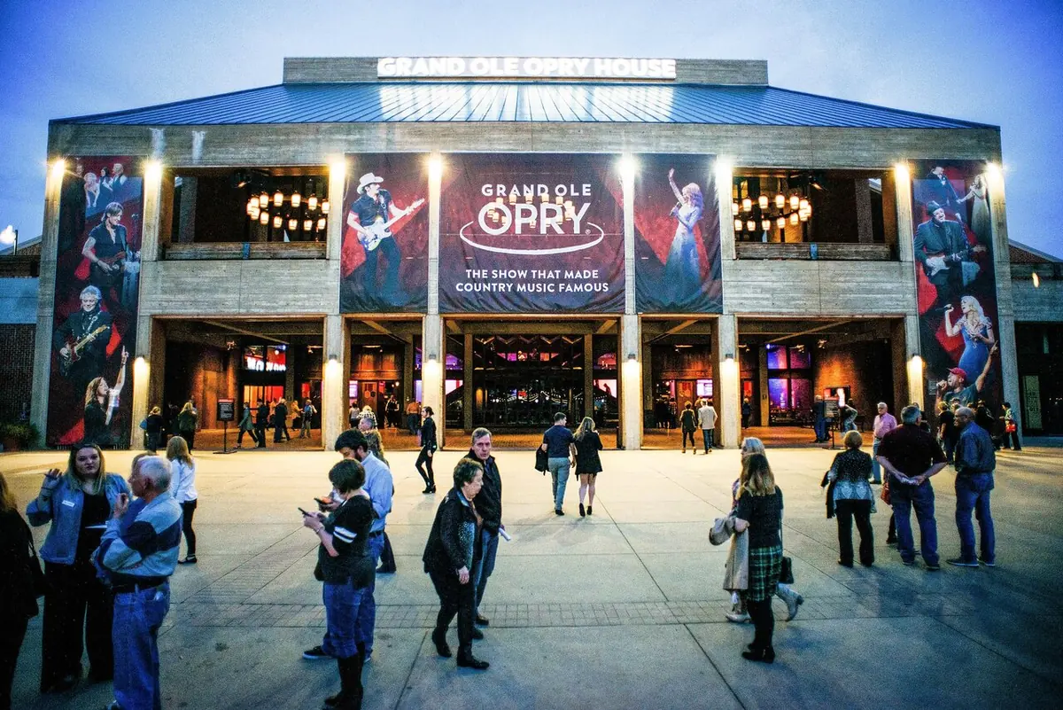 The front of the Grand Ole Opry House at dusk with large artist banners and visitors outside