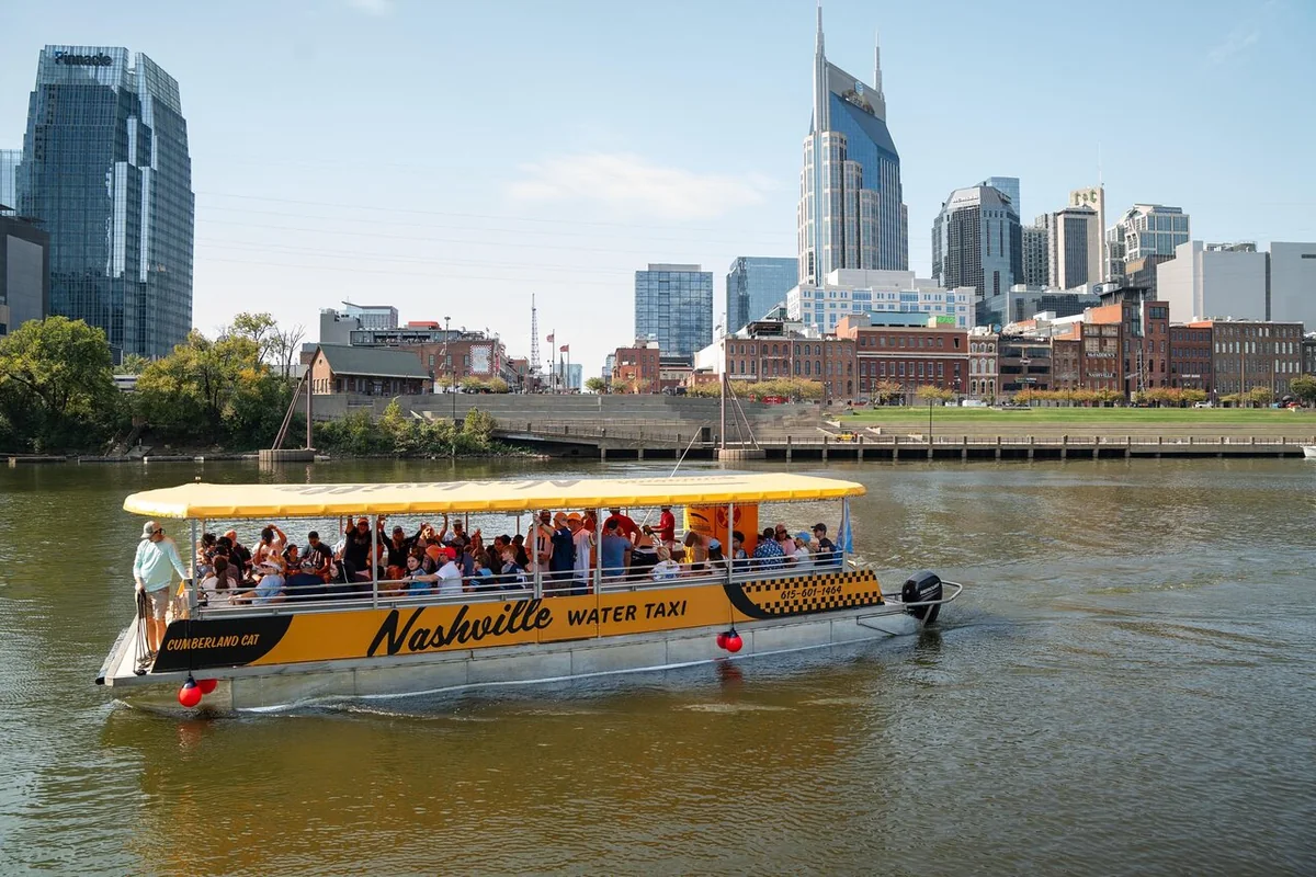 Ein gelber Ponton des Nashville Water Taxi voller Fahrgäste vor der Skyline der Innenstadt