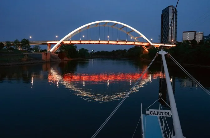 Un ponte ad arco illuminato riflesso nel fiume di notte, visto dalla prua di una barca