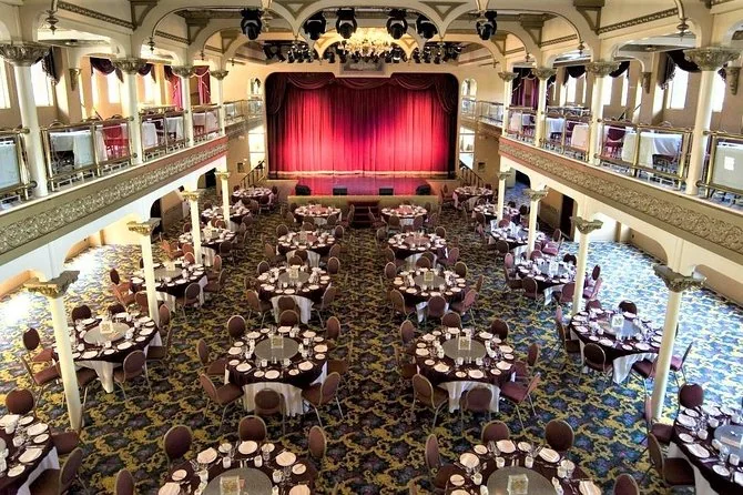 La sala da pranzo del teatro vittoriano a due piani con tavoli rotondi e un sipario rosso